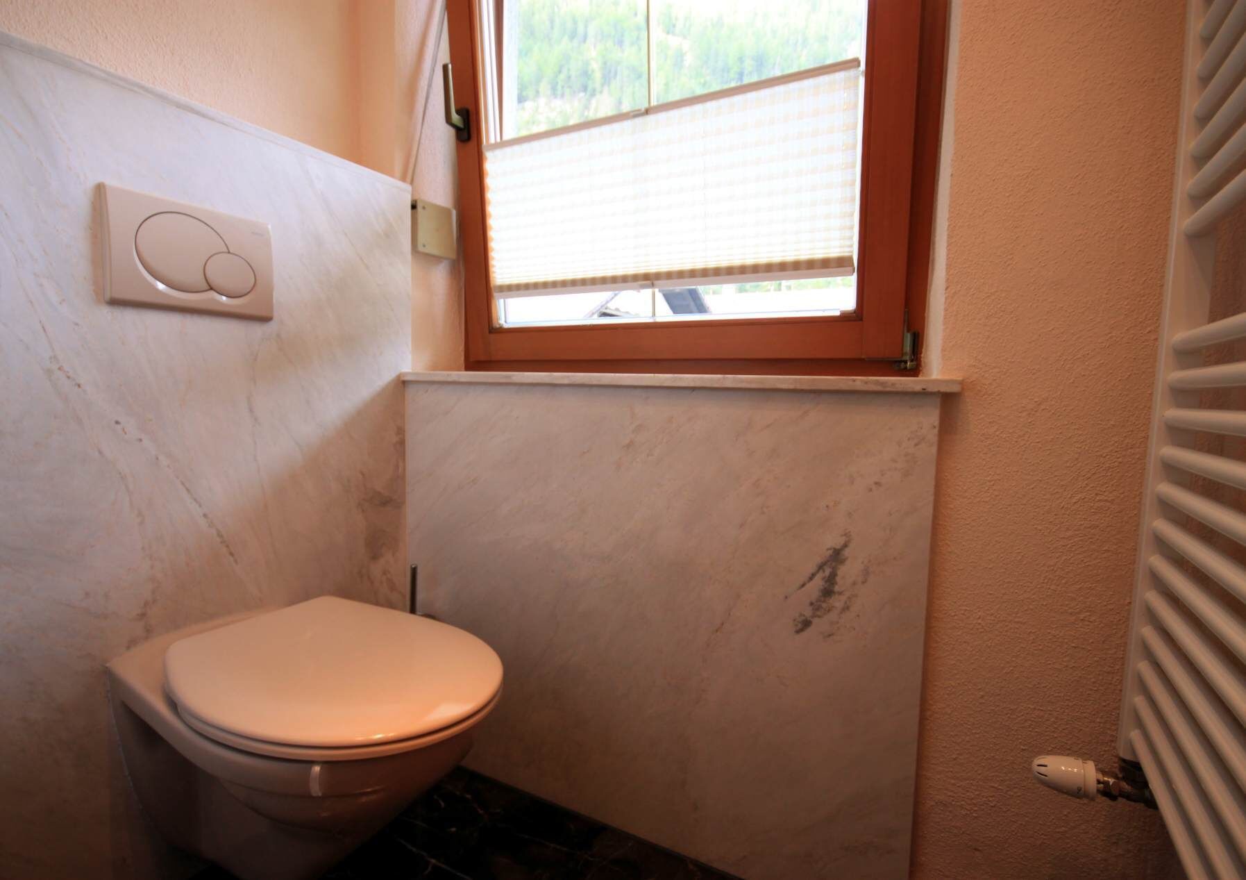 A small bathroom with a toilet, a window, and a radiator.