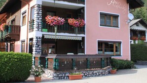 A two-story building with balconies adorned with flowers, a stone facade, and a mountain backdrop. - Haus Hrabovsky (Laengenfeld)