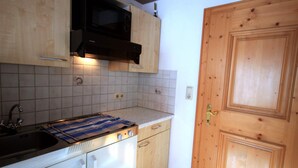 A compact kitchen with white cabinets, a black microwave, a stove, and a wooden door. - Haus Hrabovsky (Laengenfeld)