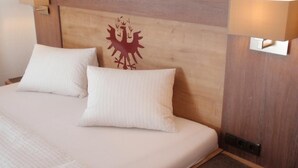 A bed with two pillows, a wooden headboard with a coat of arms, and bedside lamps. - Haus Hrabovsky (Laengenfeld)