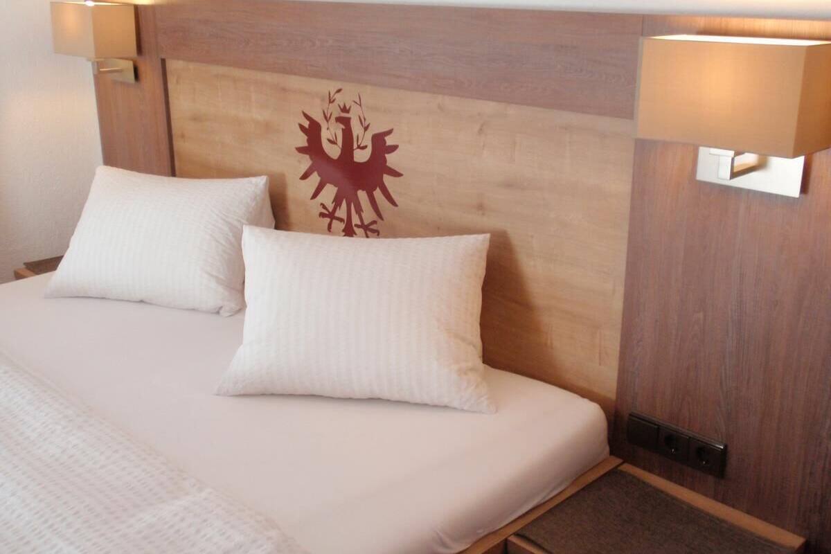 A bed with two pillows, a wooden headboard with a coat of arms, and bedside lamps.