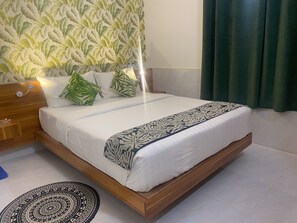 A neatly made bed with a patterned bedspread, a wooden headboard, and a wall with a leafy wallpaper pattern.