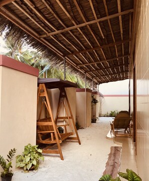 A covered outdoor area with a wooden swing, potted plants, and a chair.
