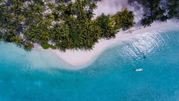 An aerial view of a beach with white sand, clear turquoise water, and dense palm trees. - Sands Inn (Mathiveri)