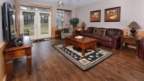 A living room with a wooden coffee table, a brown leather sofa, and a TV on a wooden stand. - 3204 Golf View Hillcrest Mountain Sanctuary (Pigeon Forge)