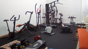 Ein Heim-Fitnessraum mit verschiedenen Trainingsgeräten, darunter Laufbänder, ein Crosstrainer und Kurzhanteln.