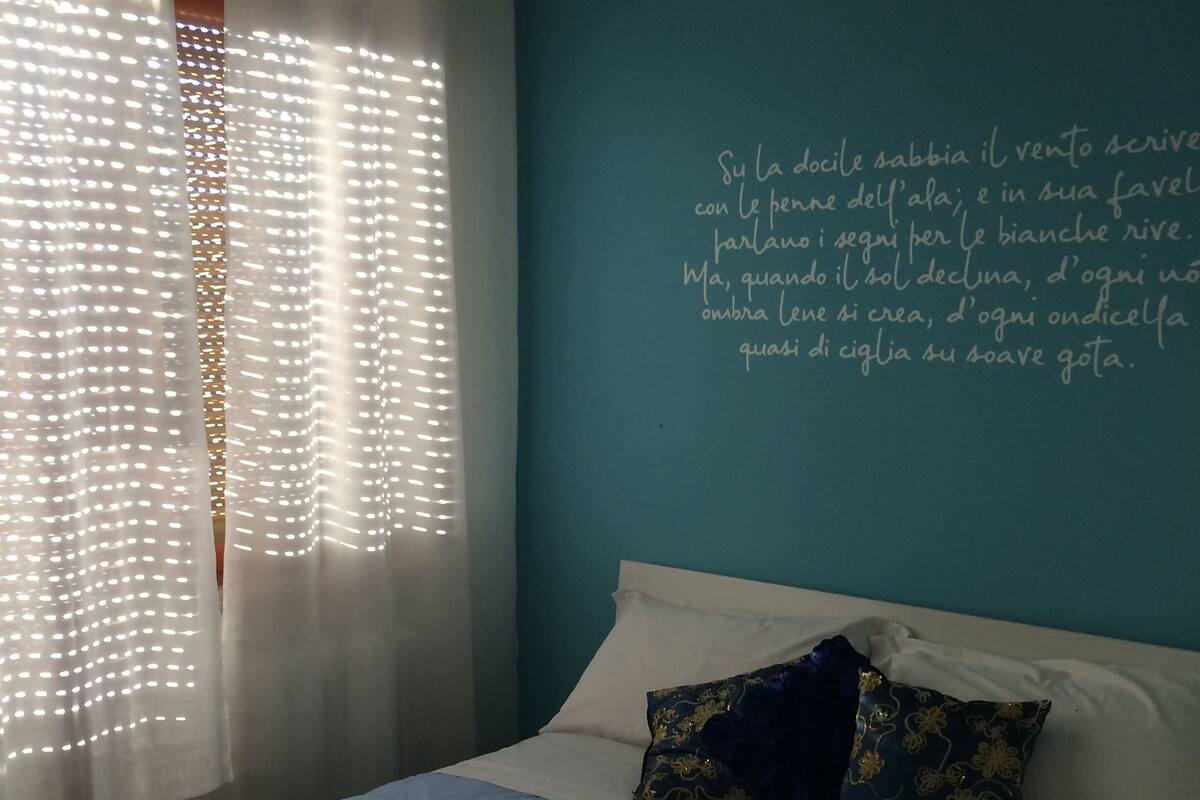 A bedroom with a bed, pillows, and a wall with a quote in Italian.