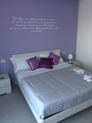 A neatly made bed with a grey bedspread and two purple pillows, a white nightstand with a lamp, and a wall with a motivational quote in Italian. - Terrazze Dannunziane (Pescara)