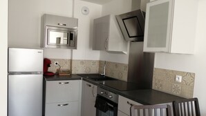 A compact kitchen with a refrigerator, microwave, oven, and a small dining area with a chair.