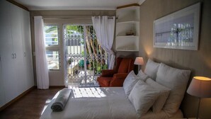 Habitación de hotel con cama, una silla, una lámpara y vistas a través de una ventana con cortinas.