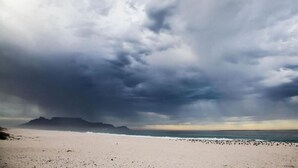 Una playa con una extensa orilla arenosa y una cadena montañosa distante bajo un cielo nublado.