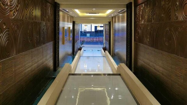 A modern hallway with a reflective floor, decorative wall panels, and recessed lighting. - ashbona hotel suites (Riyadh)