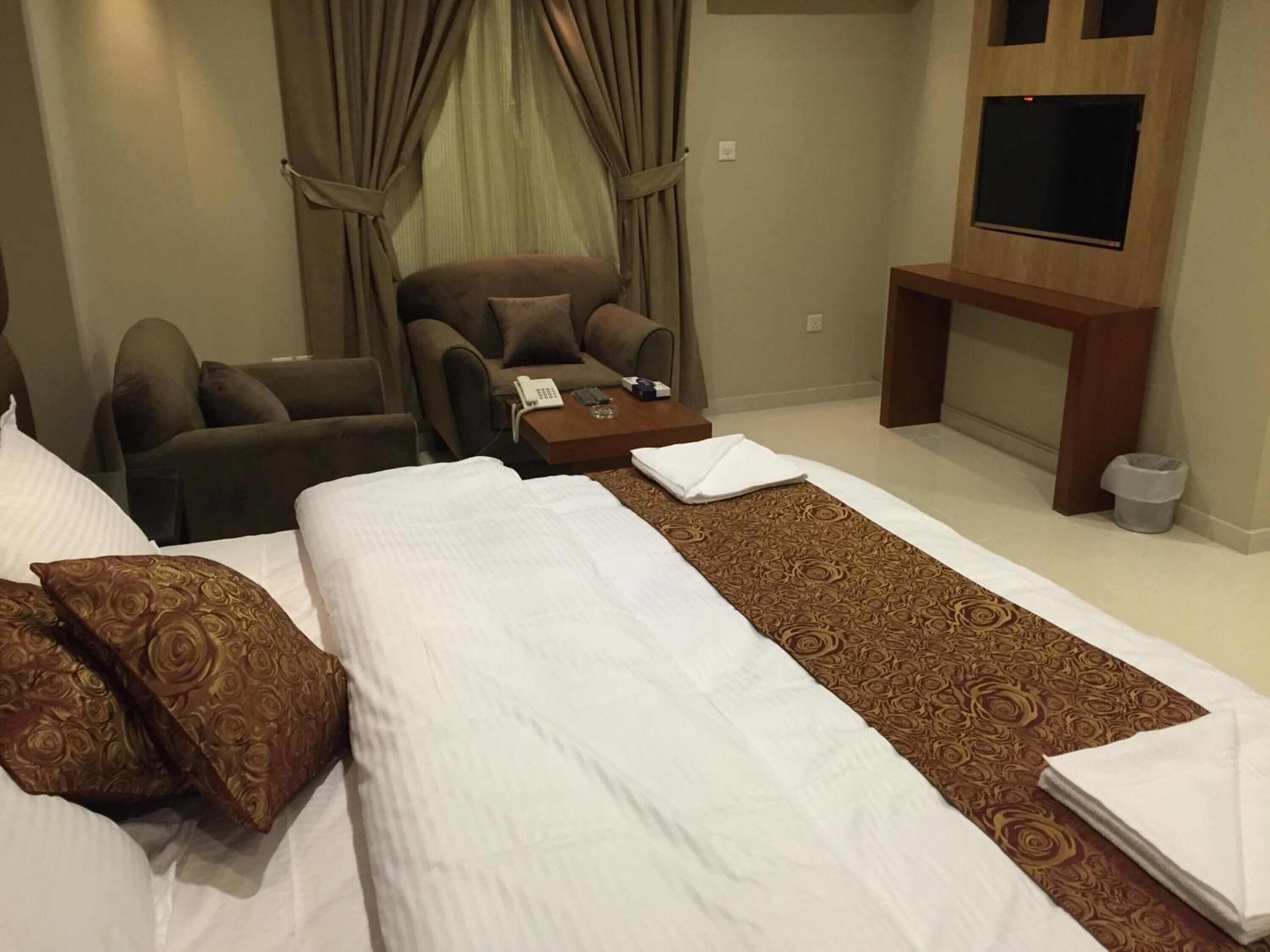 A hotel room with a bed, a sofa, a small table with a phone, and a TV mounted on the wall.