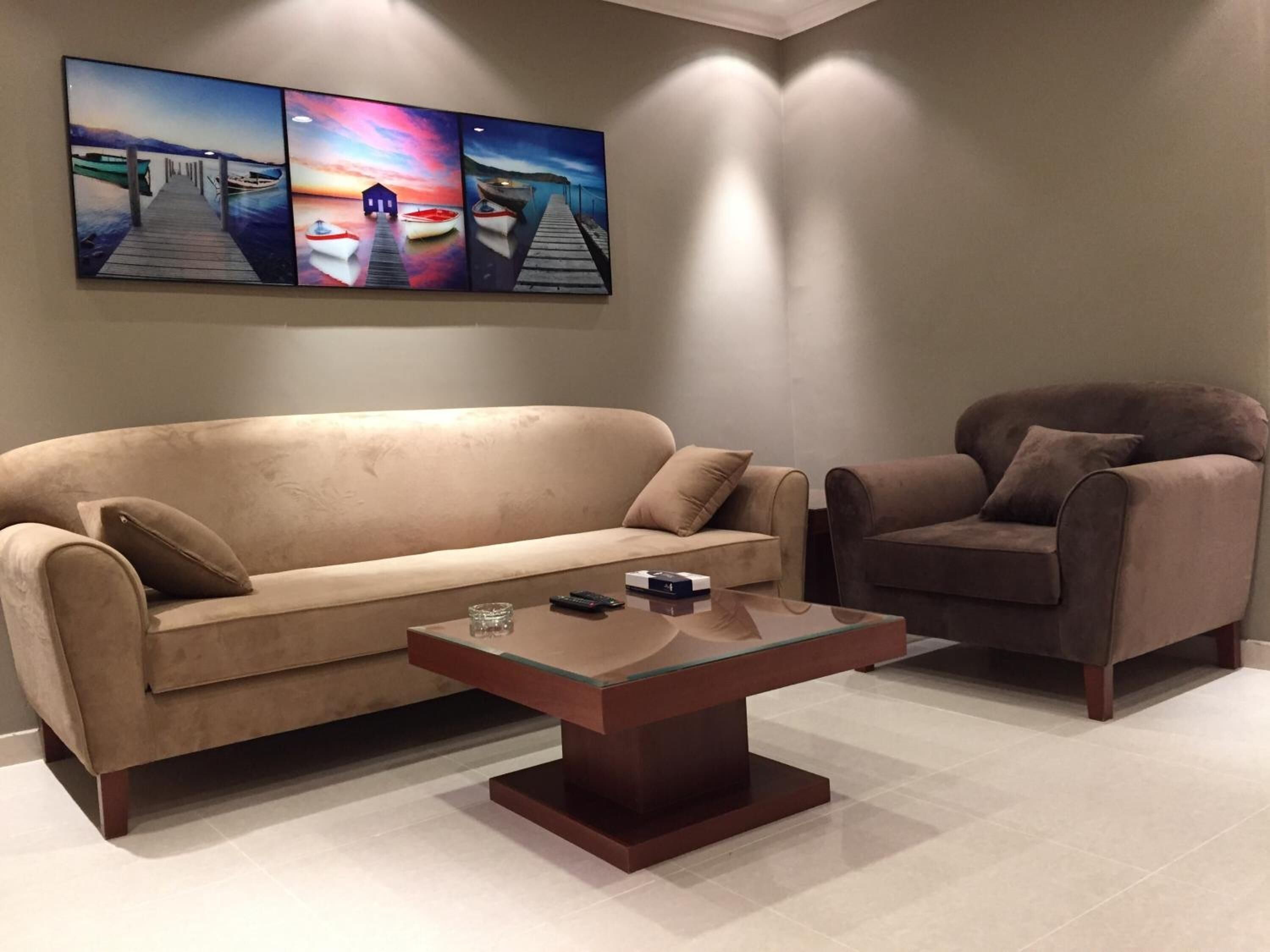 A living room with a beige sofa, a brown armchair, and a glass coffee table.
