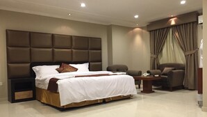 A modern hotel room with a large bed, a desk, two armchairs, and a sofa. - ashbona hotel suites (Riyadh)