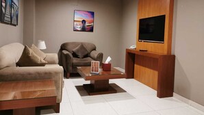 A modern living room with a sofa, armchair, coffee table, and a TV mounted on the wall. - ashbona hotel suites (Riyadh)