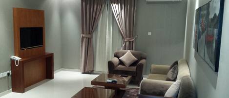 Una sala de estar moderna con un televisor de pantalla plana, un mueble de madera, una mesa de centro de vidrio y dos sofás.