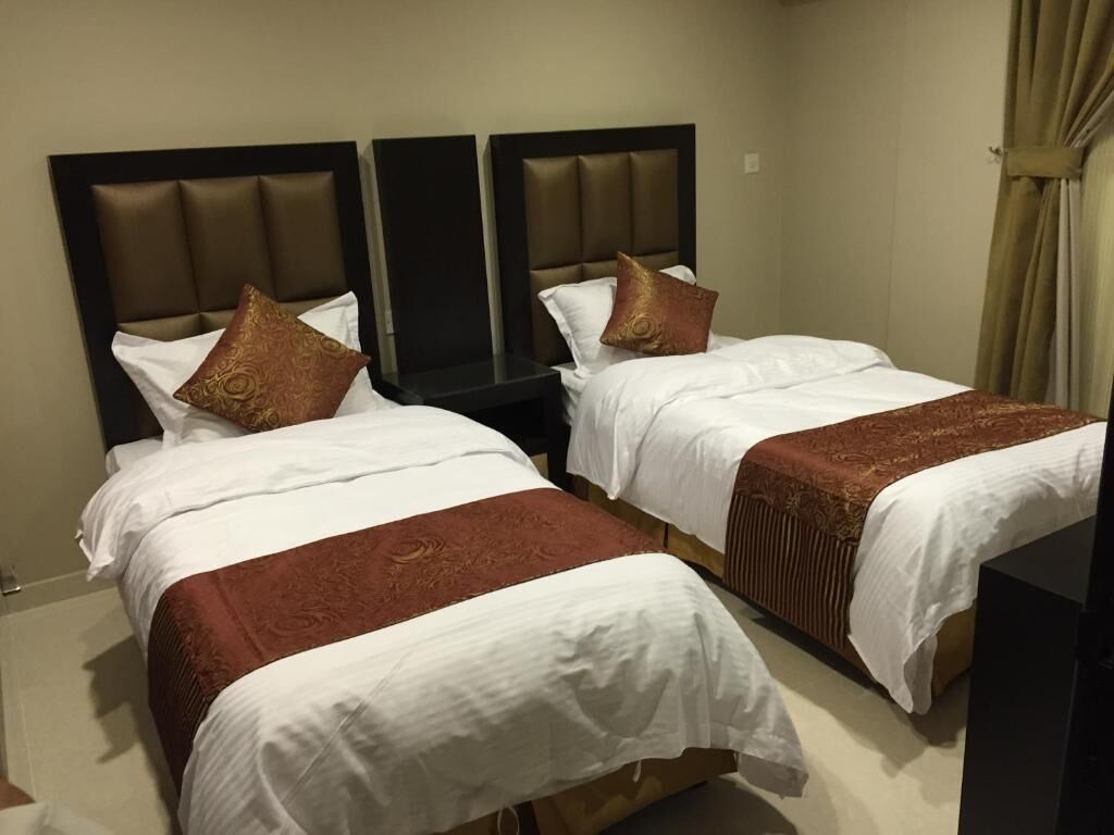 A hotel room with two beds, each with a headboard, white bedding, and a brown accent.