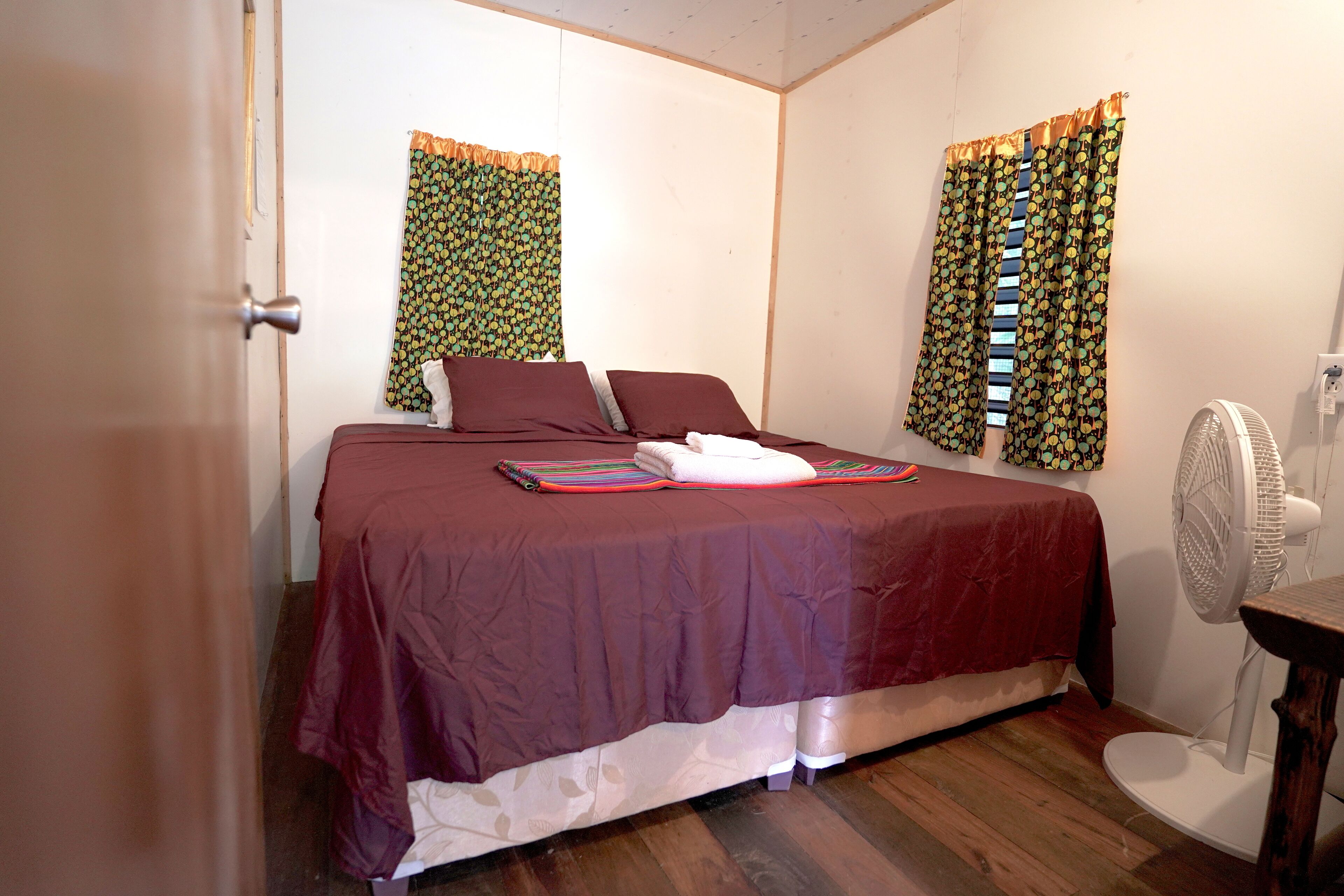 Un dormitorio con cama, cortinas, un ventilador y suelo de madera.