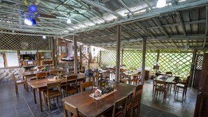 A spacious dining area with multiple wooden tables and chairs, a ceiling fan, and a view through a lattice fence. - T.R.E.E.S Research Center and Eco Lodge (Belmopan)