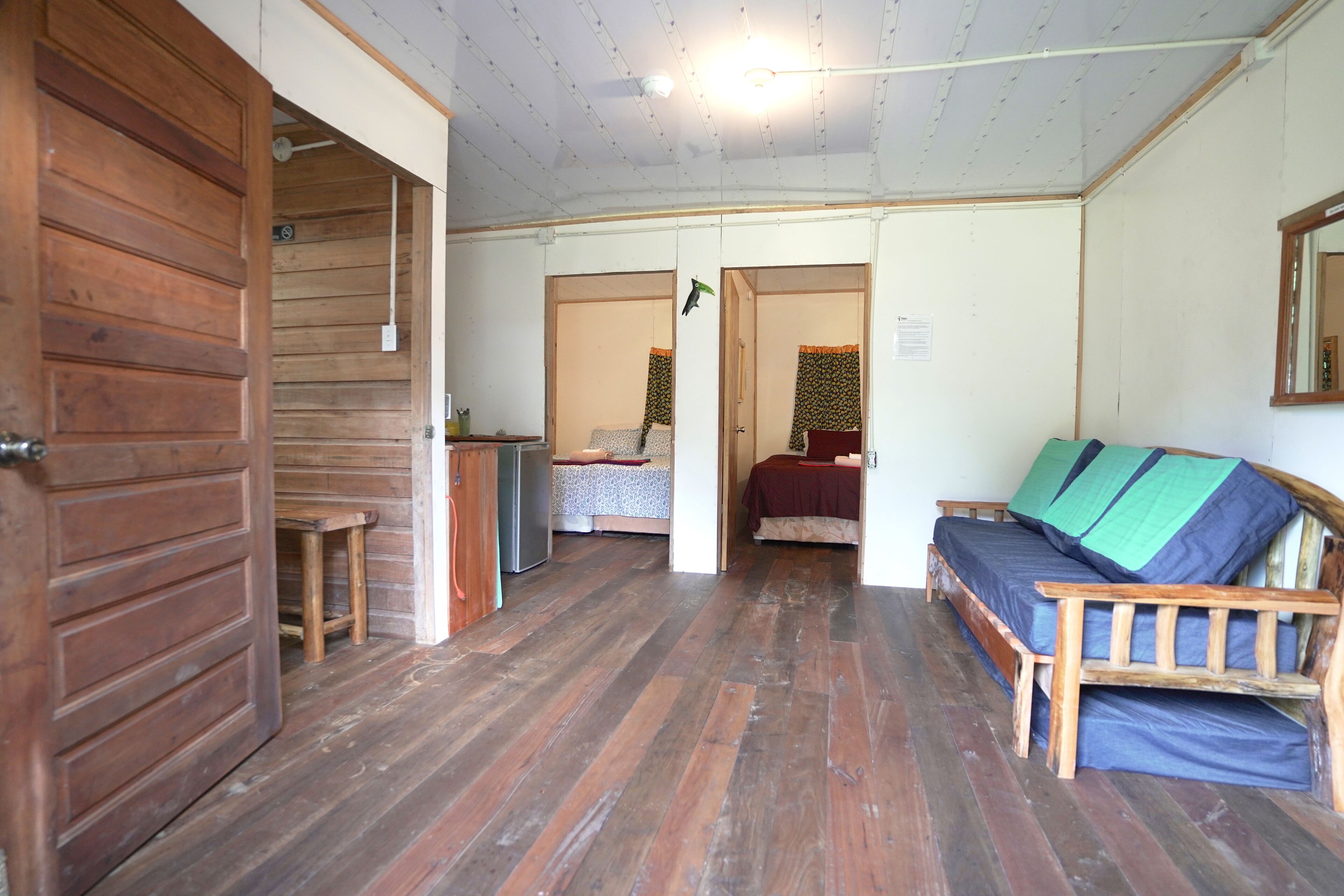 A room with wooden floors, a bed with blue bedding, a wooden bench, and a small table.