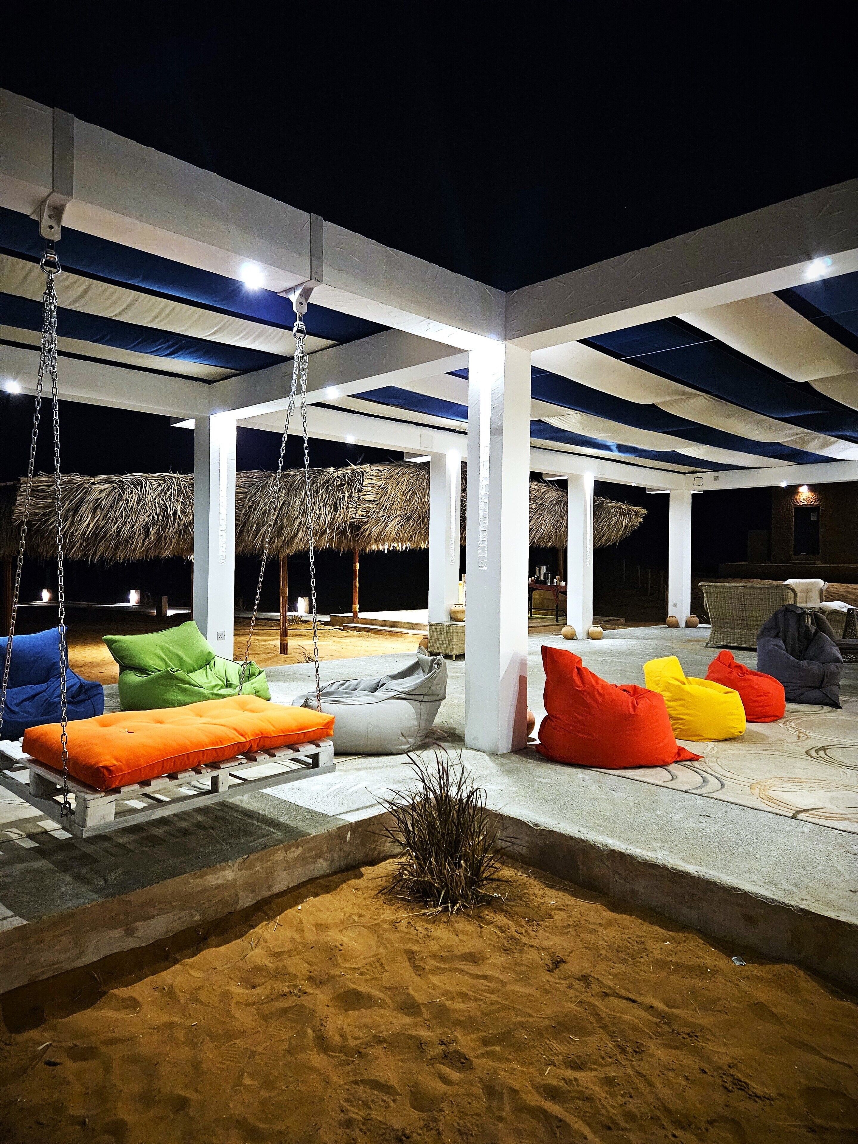Un espacio al aire libre cubierto con sillones orejeros de colores y un conjunto de columpios.