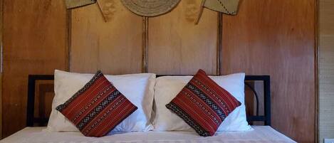 Una cama con sábanas blancas y dos almohadones decorativos con diseños geométricos.