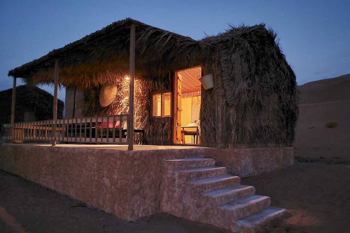 A thatched-roof hut with a stone base and a set of stairs leading up to it.