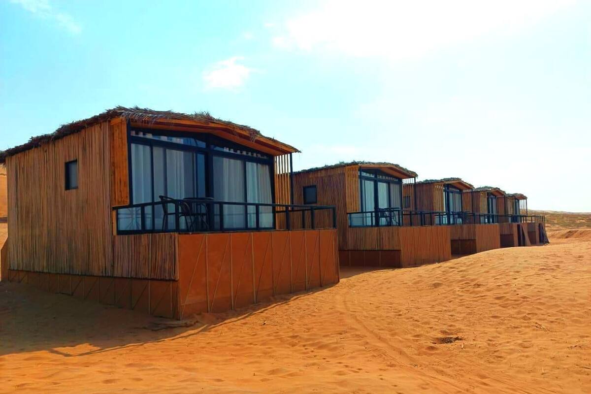 A row of wooden cabins with large windows and balconies, situated in a desert environment.