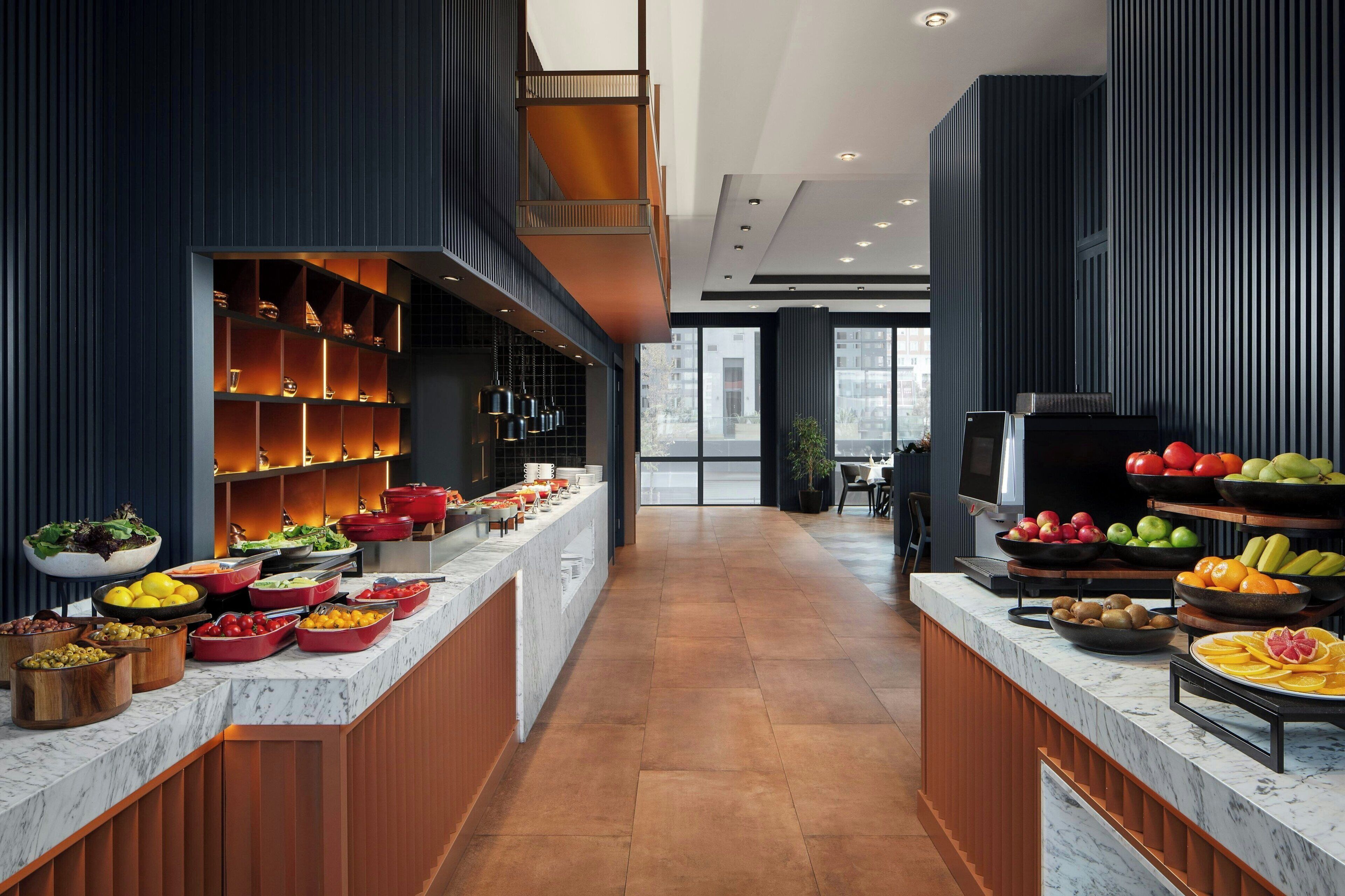 A modern kitchen with marble countertops, wooden cabinets, and a variety of food items displayed.