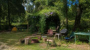 An outdoor seating area with a rustic wooden table, chairs, and a barbecue grill.