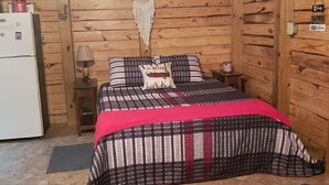 Een gezellige kamer met een bed, een tafeltje, een lamp en een koelkast.