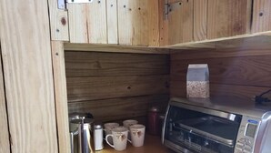Een compact keukenhoekje met een magnetron, een koffiezetapparaat en verschillende mokken op een houten aanrecht.