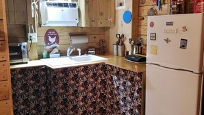 Een kleine keuken met houten kastjes, een spoelbak, een koelkast en een behangetje met patroon.
