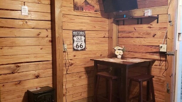 Een rustieke kamer met houten wanden, een houten tafel met twee stoelen, een aan de muur bevestigde televisie en een bordje met de tekst 'Historic Old Route 66'.