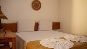 Habitación de hotel con una cama, cabecera de madera, mesita de noche con lámpara y toallas dispuestas sobre la cama.