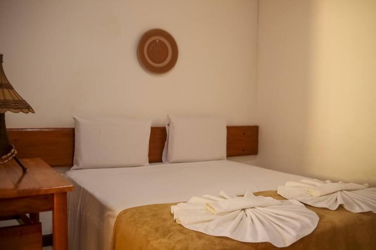 A hotel room with a bed, a wooden headboard, a bedside table with a lamp, and towels arranged on the bed.