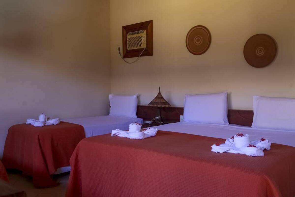 A hotel room with two beds, each with a red bedspread and white pillows. There is a wall-mounted radio and two decorative wall plates.