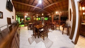Un espacio interior amplio con mesas y sillas de madera, una barra y un televisor montado en la pared.