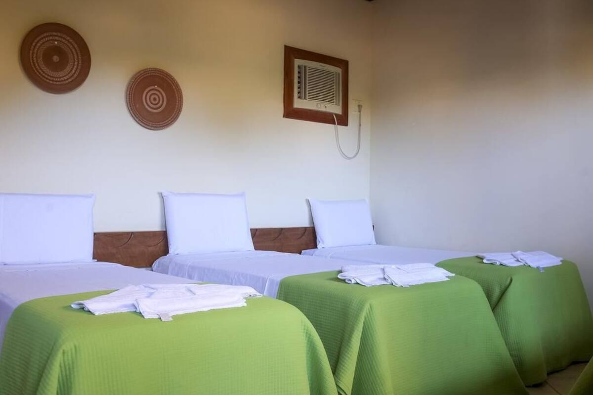 A hotel room with two single beds, each with green bedspreads and white pillows, and a small table with folded towels.