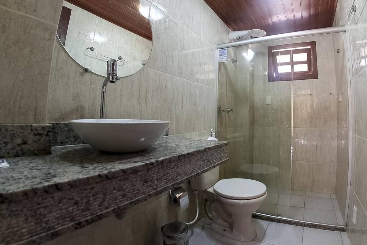 A bathroom with a granite countertop, a white sink, a mirror, a toilet, and a glass-enclosed shower.