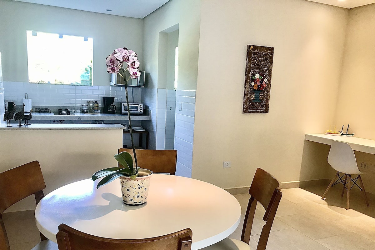 Una cocina moderna con armarios blancos, una mesa de comedor con sillas y una orquídea en maceta.