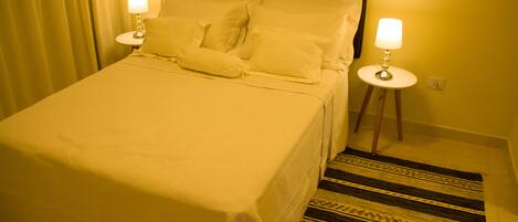 A hotel room with a bed, two bedside lamps, a patterned rug, and a headboard.