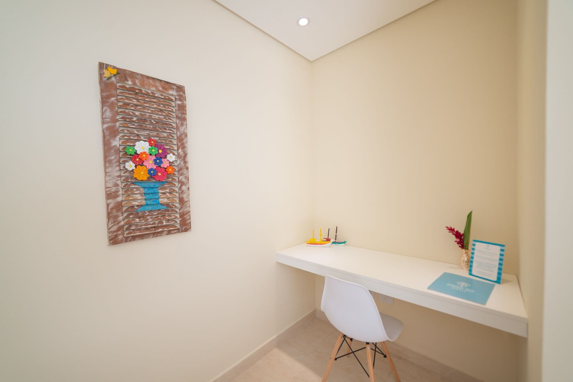A clean, modern room with a white desk, a small plant, and a colorful artwork on the wall.