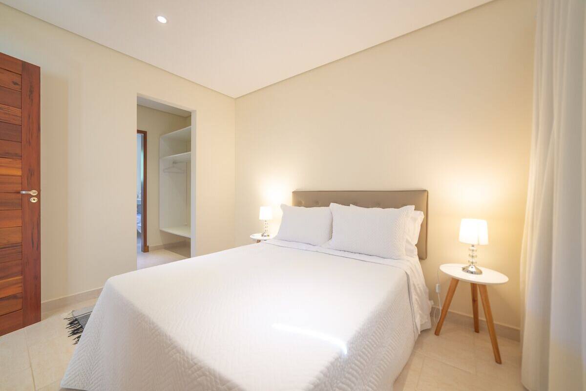 Una habitación de hotel ordenada con una cama grande, dos mesitas de noche con lámparas y una puerta de madera.
