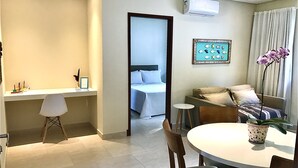 Une chambre d’hôtel moderne comprenant un coin repas, un lit et une salle de bain, le tout visible à travers une porte ouverte.