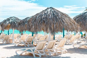 Beach chairs arranged under thatched umbrellas on a sandy beach. - Pool Terrace, Deluxe E1, Close to Beach, 2Br, 2Bt (Bávaro)