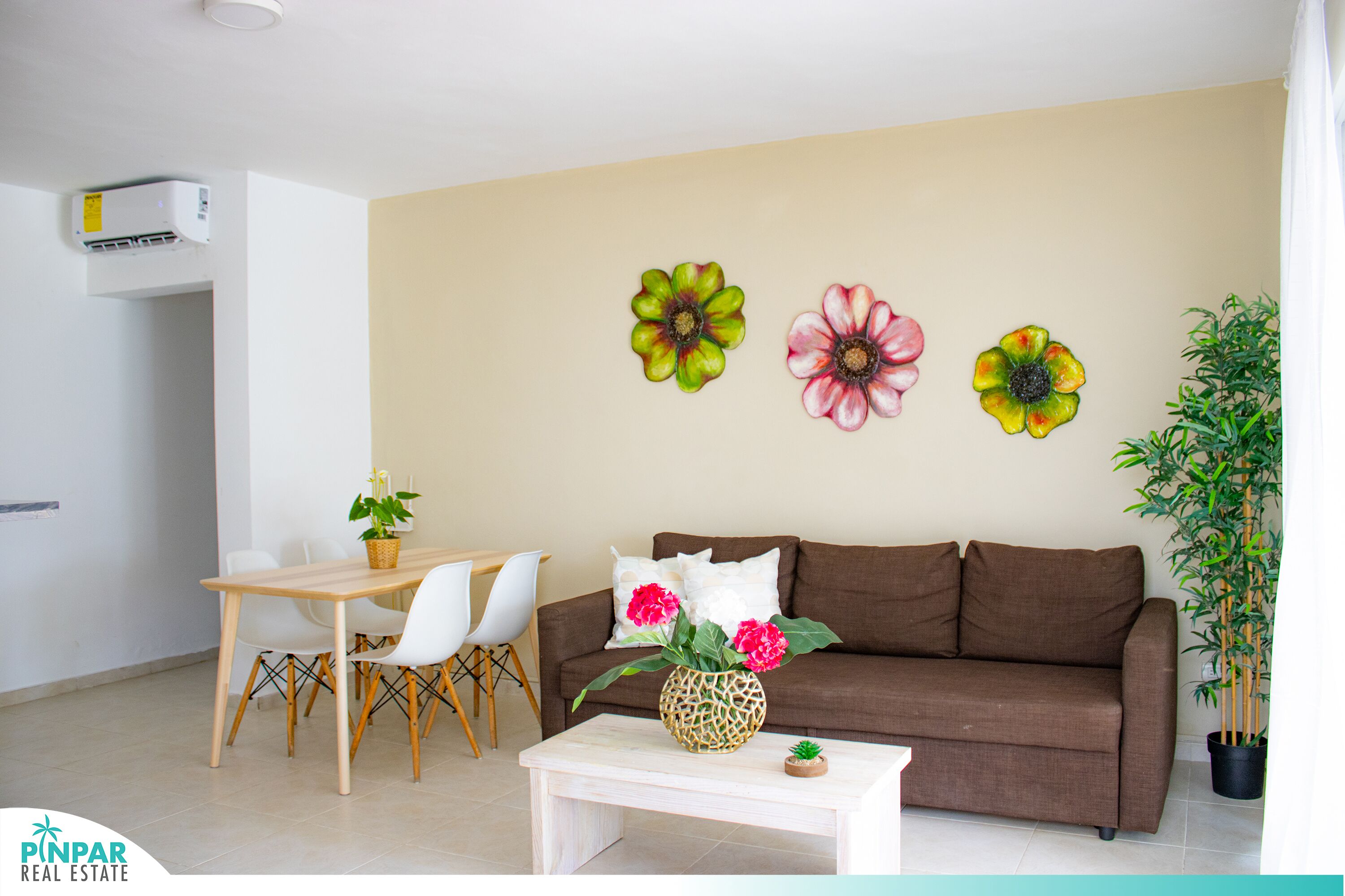 Een woonkamer met een bruine bank, witte stoelen, een houten salontafel en een plant in pot.