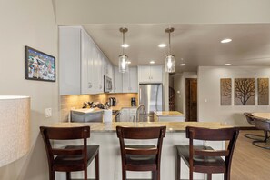 A modern kitchen with white cabinets, stainless steel appliances, and pendant lighting.
