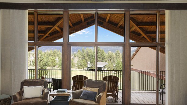 Una habitación amplia con ventanas grandes, techo de madera y dos sillones de cuero.